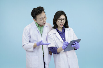 Astonished Asian science professionals reacting to a breakthrough, excitedly viewing data on a digital tablet during research in blue studio background