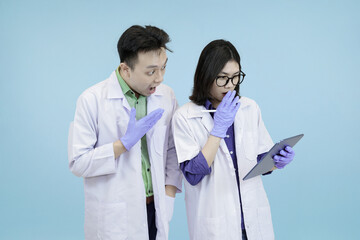 Astonished Asian science professionals reacting to a breakthrough, excitedly viewing data on a digital tablet during research in blue studio background