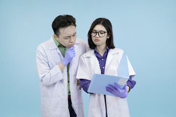 Two Asian medical or science professionals discussing research, actively debating data shown on a digital tablet studio blue background