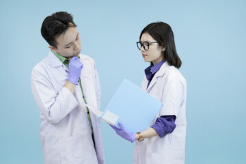 Pensive Asian science professionals closely examining data on a digital tablet, symbolizing focused analysis and problem-solving during research in studio blue background