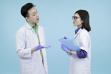 Two Asian medical or science professionals discussing research, actively debating data shown on a digital tablet studio blue background