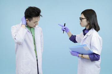 An assertive Asian female scientist reprimanding a male colleague, pointing a pen at him while he looks stressed over a mistake in blue studio background