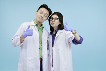 Cheerful Asian science professionals giving enthusiastic thumbs-up gestures, symbolizing success, approval, or excellent research results in blue studio background