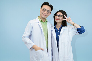 Friendly Asian science professionals giving peace or victory signs, symbolizing hope, safety, or successful research outcomes in studio blue background