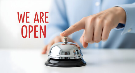 Finger presses a shiny silver service bell on a white counter with a red "we are open" sign indicating business is ready for customers and welcoming guests to come in and enjoy the services offered no