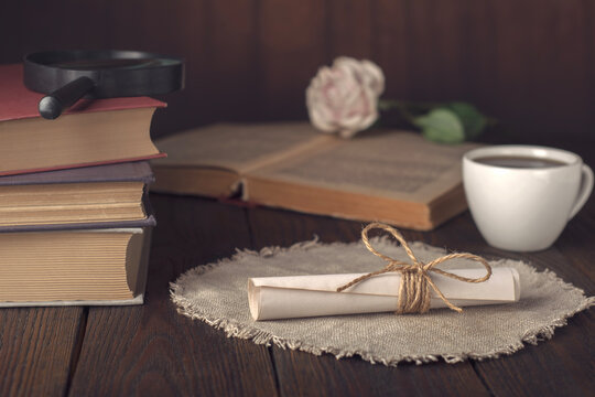 Vintage scroll tied with linen twine on a textured linen cloth, surrounded by old books, an open book with a rose, a cup of coffee, and a magnifying glass