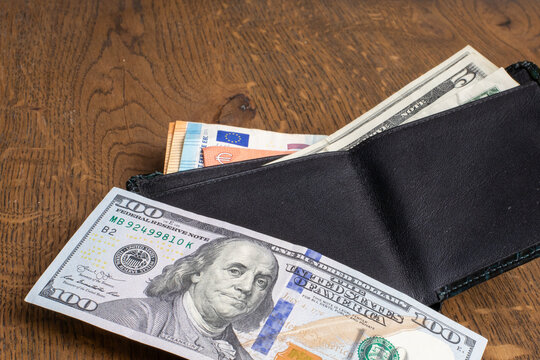 Banknotes of USD and EUR partially visible in black wallet placed on wooden surface. Finance, savings, daily expenses and currency exchange. Real photo