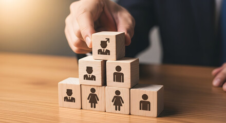 Hand places wooden block with graduate icon atop a pyramid of blocks representing team members symbolizing career growth and leadership development in a business setting
