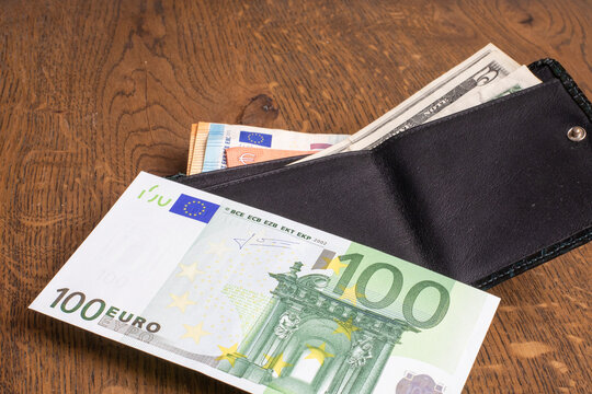 Black leather wallet with 100 Euro and US Dollar bills on wooden surface. Finance, currency, personal budget. Real photo