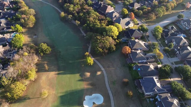Central fairway of Lantana Golf Club winds between tree buffers and residential blocks. Mowing lines, pools, paved paths highlight the harmony of leisure and suburban zoning, mansion homes, Texas