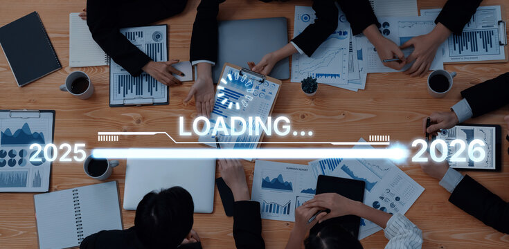 A diverse group of professionals engage in a business meeting, analyzing charts and data projections for 2025 and 2026 displayed on digital devices. Trope