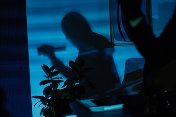 Silhouette of young adult man holding flashlight projected on office wall, shadow suggesting...