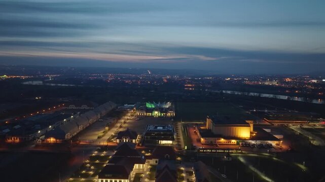 Night aerial view over the Ostra area in Dresden with the illuminated Ostra Dome and exhibition halls, surrounded by the wide city panorama and the Elbe in the background.
