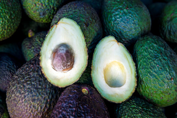 fresh avocados displayed in a pile with two halves showing their seed and creamy flesh, highlighting the texture and natural green color of the fruit in a market setting