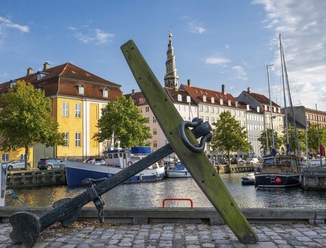Old anchor, sailing boats, historic buildings and tower of Vor Frelsers Kirke or Church of the Saviour, Christianshavn Canal, Copenhagen, Denmark