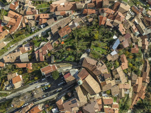 Aerial view of terracotta rooftops cascading down the gentle slopes, punctuated by verdant trees, creating a tapestry of warm hues and natural beauty, Capocastello, Irpinia, Italy.