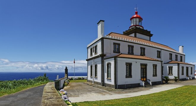 A white lighthouse with red roofs and a display by the sea under a clear blue sky, Farol da Ferraria lighthouse, Sao Miguel Island, Azores, Portugal