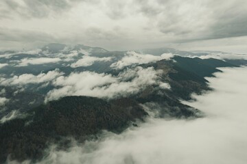 Above the Piatra Craiului Mountains, a drone captures the mystical beauty of clouds shrouding the rugged peaks, creating a serene and enchanting atmosphere in Romania