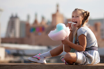 Little blonde girl with colorful braids eating vibrant cotton candy outdoors