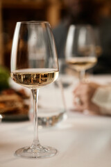 Caucasian woman hand holding wine glass while tasting wine at table, another wine glass and blurred figure in background suggesting wine tasting session