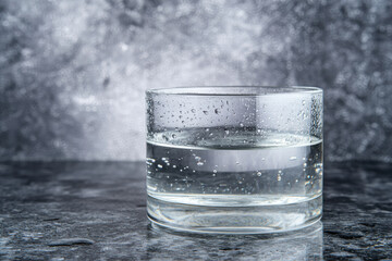 Glass of sparkling water on wet stone surface with water droplets and soft bokeh background, refreshing beverage mood