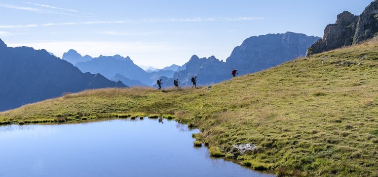 Group of mountaineers in front of mountain landscape, mountain lake and silhouettes of rocky mountain peaks, Luggauer T&ouml;rl, Carnic High Trail, Carnic Main Ridge, Carnic Alps, Carinthia, Austria