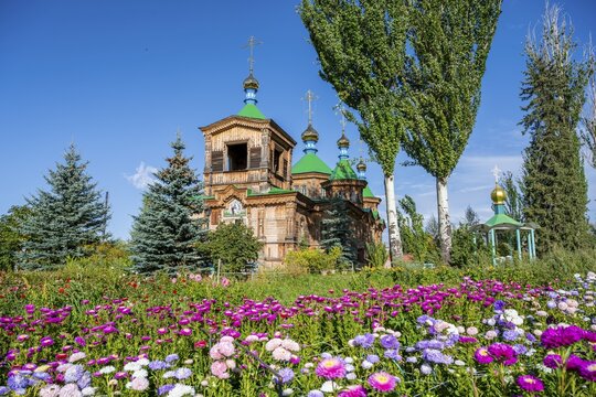 Colourful flowers in front of the Russian Orthodox Church Cathedral of the Holy Trinity, wooden church with green spires, Karakol, Kyrgyzstan