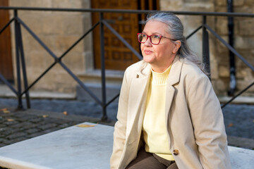 Older woman enjoys a peaceful moment sitting on a stone bench in a charming, historic street during...