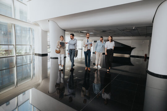 A team strolls through a sleek office lobby, discussing plans. The polished black floor, bright glass walls, and contemporary design create a professional, collaborative mood.