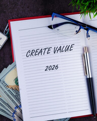 Open notebook with lines displays Create Value and 2026, resting beside money, glasses, and a pen. Greenery and office supplies subtly add to the scene
