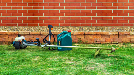 Brush cutter or shoulder strap mower and green gallon of gasoline on lawn with green grass before cutting. Petrol brush cutter, grass cutting. Backpack mower or lawn mower for mowing grass and shrubs.