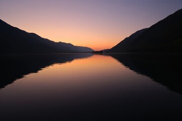 Calm lake reflects the sunset between mountains creating a peaceful and beautiful landscape view