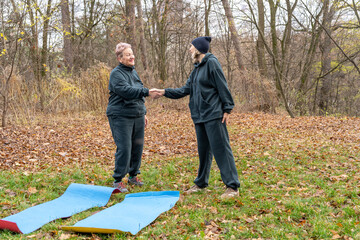 Two Senior Women Shaking Hands Outdoors before Fitness Training in autumn park nature. Sport exercise trainer