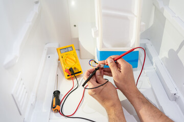 Close-up of an electrician repairing a refrigerator power outlet and measuring the voltage with his...