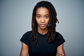 Portrait of a woman with dreadlocks wearing a black shirt against a gray background and arms crossed