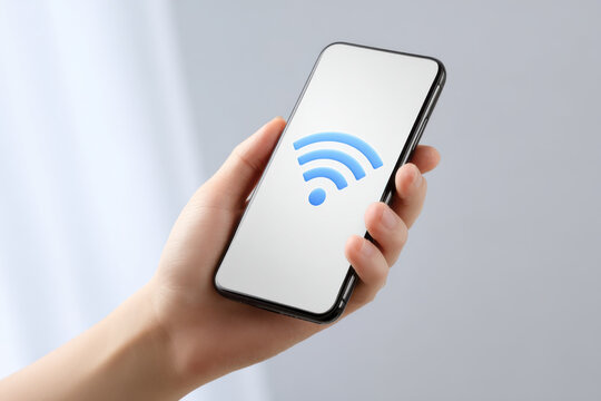 Smartphone held in hand showing blue wireless internet symbol on screen with soft background light
