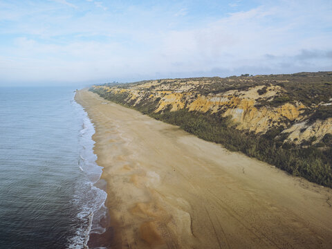 Aerial view of Playa Torre del Loro's golden sands meeting the endless blue ocean under a serene sky, Mazagon, Andalusia, Spain.