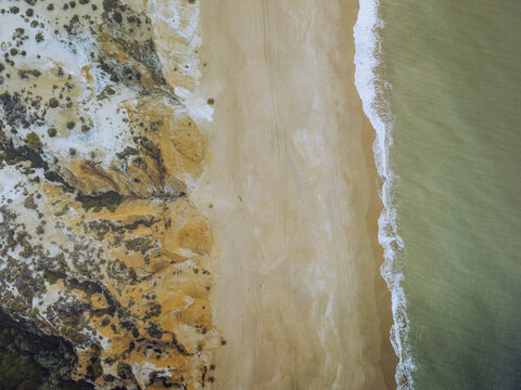 Aerial view of golden sands meeting the restless turquoise sea next to the rugged cliffs of Playa Torre del Loro, Mazagon, Andalusia, Spain.