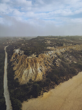 Aerial view of the rugged coastline where golden cliffs meet the verdant shrubbery, overlooking the sandy beach, Mazagon, Andalusia, Spain.