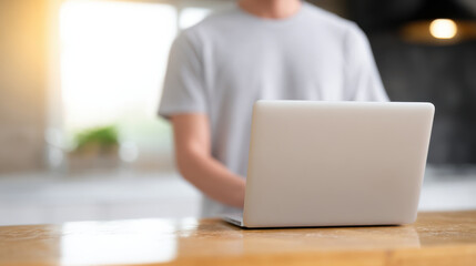 Person working on laptop at wooden table with blurred background and warm sunlight