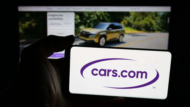 Stuttgart, Germany - 11-14-2025: Person holding mobile phone with logo of automotive classifieds company Cars.com Inc. on screen in front of web page. Focus on phone display.