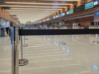 Close up of black belt barrier queue line at empty airport check-in terminal with blurred background.