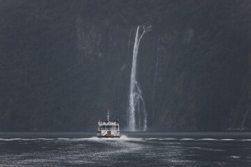 Milford Sound, New Zealand - May 20, 2025: A cruise ship sails past a massive waterfall and sheer,...