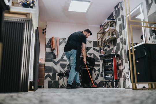 A focused man cleans a modern bathroom, using a mop near a rolling tool cart and towels. Geometric tile walls, organized equipment, and a bright ceiling light create a professional cleaning scene.