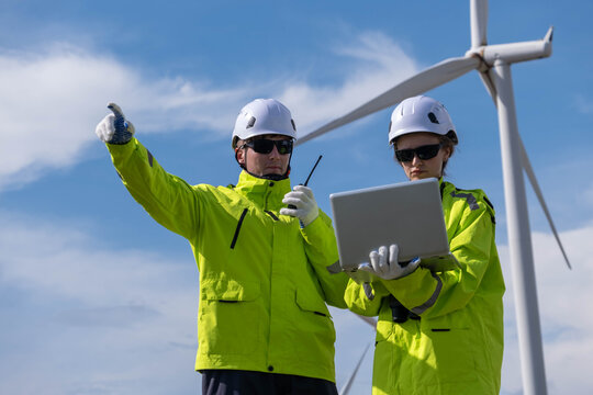 Workers inspect wind turbines while reviewing data and communicating on a sunny day in a renewable energy field