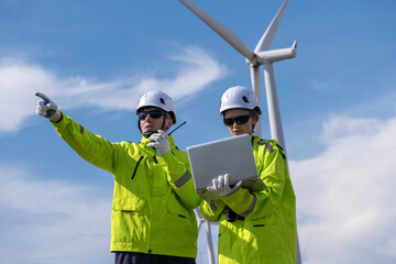 Wind energy technicians inspect turbine operations while communicating and analyzing data in bright safety gear