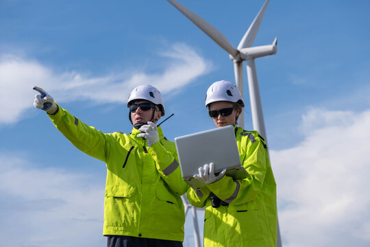 Wind energy technicians inspect turbine operations while communicating and analyzing data in bright safety gear