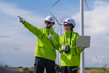 Engineers discussing plans at a wind farm with turbines in the background on a clear day