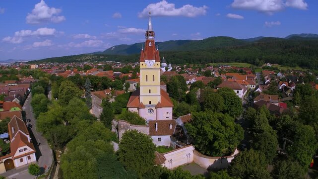 Aerial footage over Cristian village in Brasov county, Transylvania, Romania, with Saxon Evangelical church tower, red-roofed houses and hills on a bright summer day, peaceful rural landscape