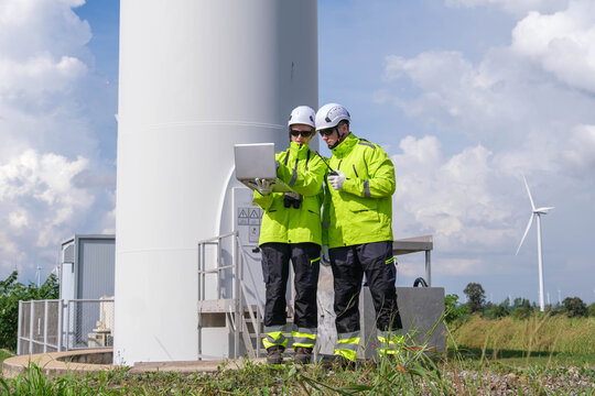 Two technicians check data on a laptop near a wind turbine in a clear, sunny environment